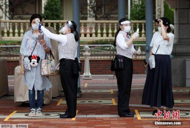 资料图：当地时间7月1日，日本东京迪士尼乐园和东京迪士尼海洋乐园恢复营业。图为游客佩戴口罩，进行体温检测。