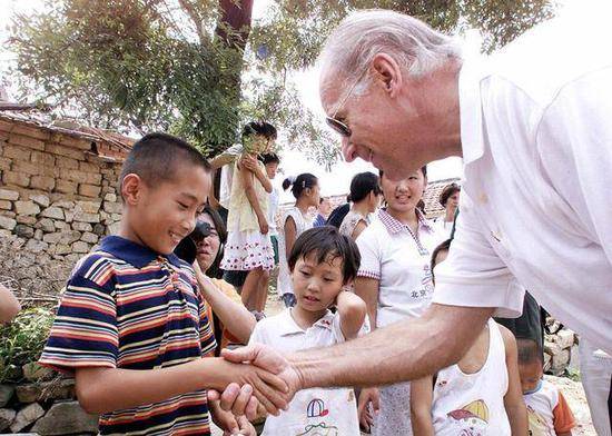 （图说：2001年8月10日，拜登访问北京北部的雁子口村时与七岁男孩高山握手。）