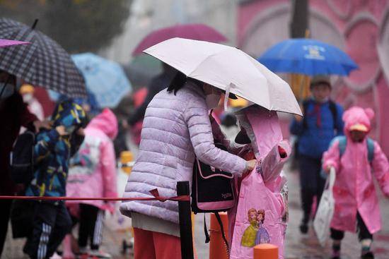 在北京怡乐中街的一所小学门前，家长为孩子穿好雨衣。