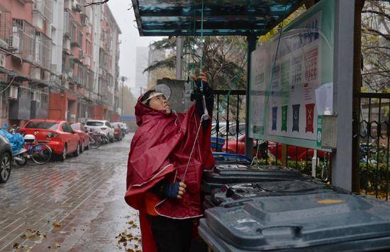 海淀区西王庄小区，一名垃圾分类指导员冒雨整理垃圾站，方便居民投放。