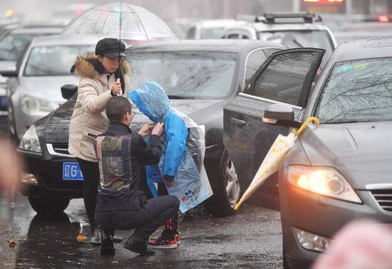 在北京怡乐中街的一所小学门前，两名家长在为一个孩子整理雨衣。