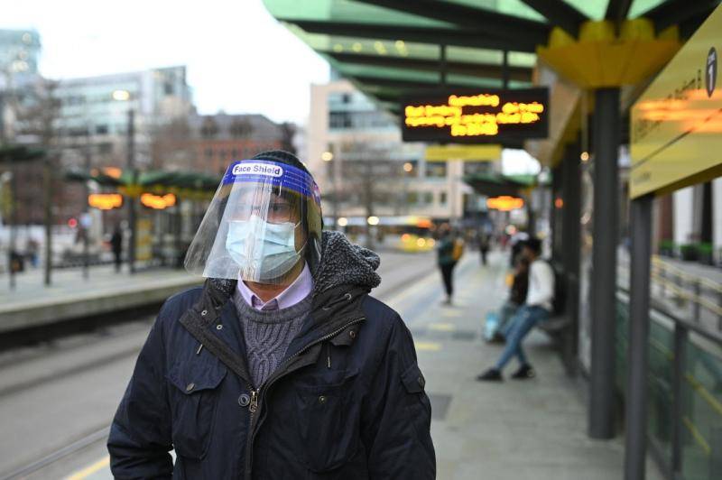 11月26日，一名佩戴口罩和防护面罩的男子在英国曼彻斯特的车站等车。新华社图