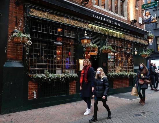 12月18日，人们走过英国伦敦的一家酒吧。图片来源：新华社韩岩摄