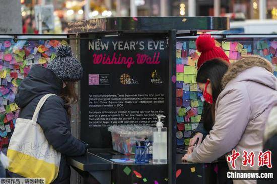 当地时间12月22日，民众在美国纽约时报广场的许愿墙旁，写下愿望。