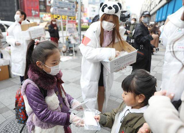 ↑2020年2月29日，在日本东京的池袋站前，在日华侨华人志愿者团体“口罩熊猫行动小组”向当地民众免费发放口罩，一名小志愿者（前左）将儿童用口罩送给日本小朋友。新华社记者杜潇逸摄