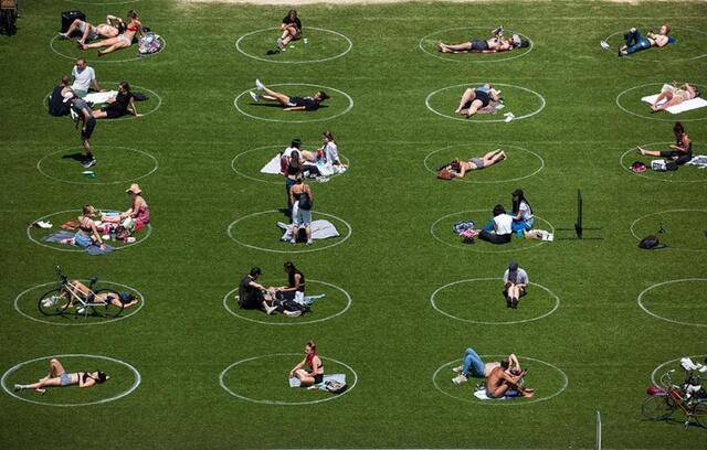 ↑2020年5月27日，人们在美国纽约室外空地休闲。地面的圆圈提示公众保持社交距离。新华社发（郭克摄）