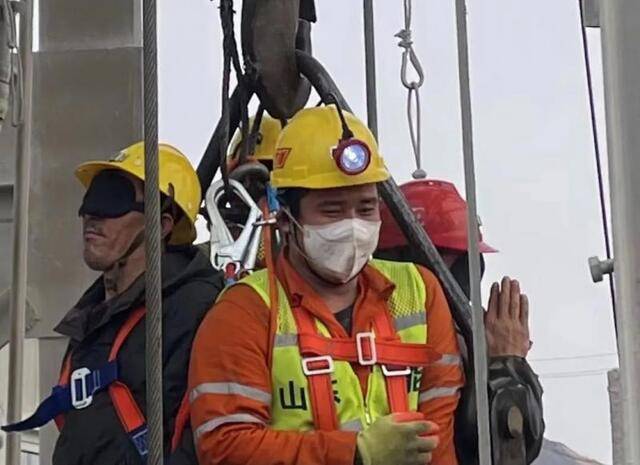 获救矿工戴着黑色眼罩升井后，一人双手合十向救援人员感谢。图片来源：烟台市委宣传部