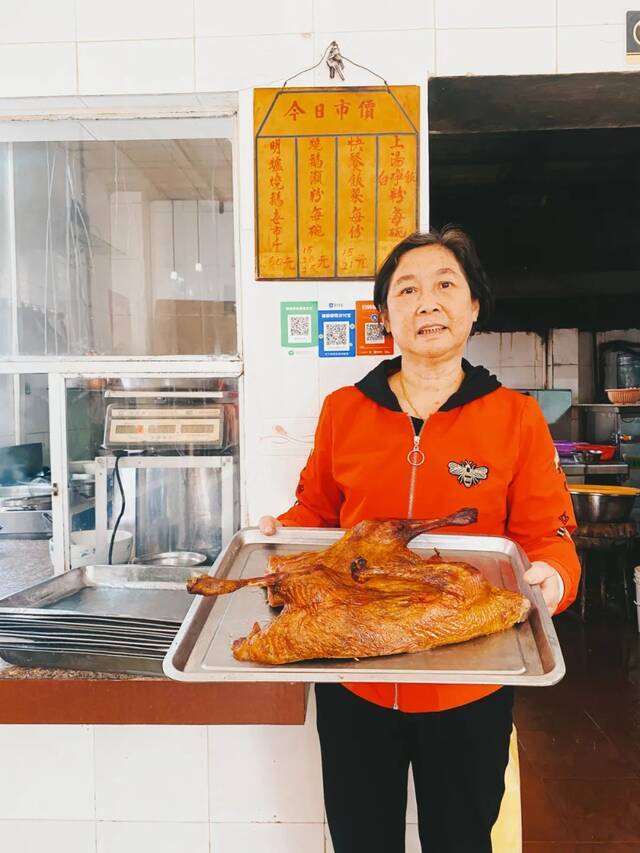 ▲63岁的华姨和她研发的烧鹅，背后的餐牌从上世纪90年代一直沿用至今