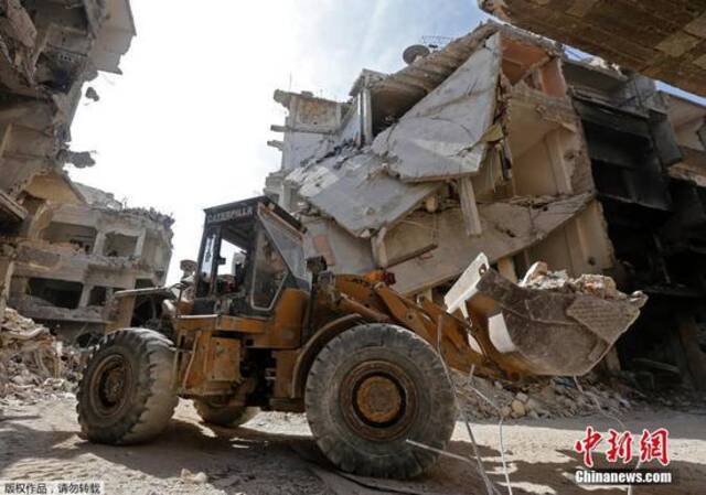 资料图：位于叙利亚首都大马士革近郊的雅尔穆克难民营展开清理工作，大型推土机和卡车开进废墟堆里清理瓦砾。