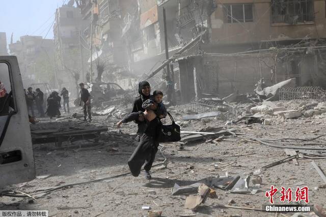资料图：当地时间2018年3月，叙利亚遭袭，一名妇女抱着孩子在废墟上狂奔。