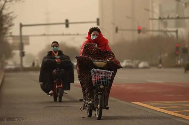 今天早上，市民顶着沙尘前行。图源：新京报网