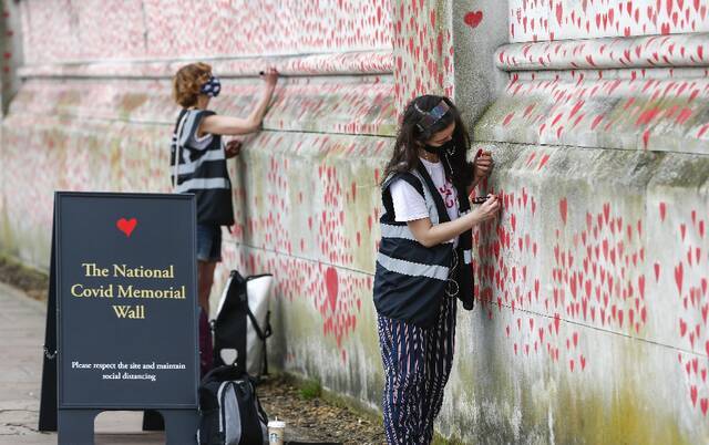 ↑志愿者在英国伦敦的国家新冠纪念墙上画红色的心