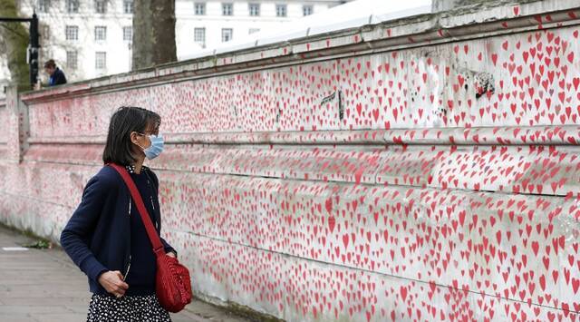 ↑3月31日，一名女子从英国伦敦的国家新冠纪念墙前走过。