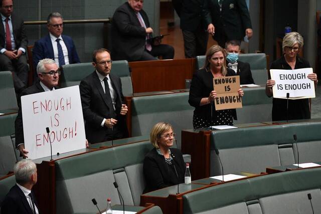 ▲澳大利亚议会成员举牌抗议：“够了”。图据《纽约时报》