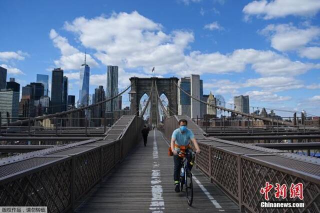 图为戴着口罩的骑手在纽约布鲁克林大桥上骑行。