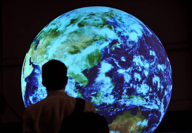 ↑这是2009年12月17日，在丹麦首都哥本哈根举行的联合国气候变化大会会场，一名与会人员站在地球模型前。新华社记者武巍摄