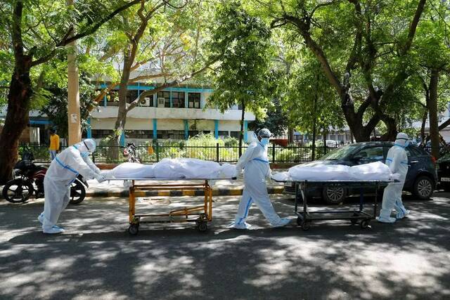 新德里一家医院外，几名医务工作者运送死于新冠肺炎的病人尸体。（路透社）