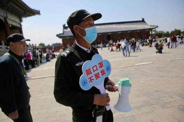 ▲5月2日，北京天坛祈年殿前，安保人员举着防疫提示牌，提醒游客戴好口罩，保持距离。当天，北京全市公园待客164万人次。新京报记者郑新洽摄影