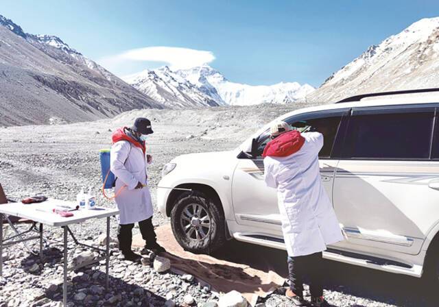 图①：近日，中国珠峰登山营地外防疫卡点的工作人员为进入营地的工作车辆消毒，并为驾驶员量体温。新华社记者王沁鸥摄