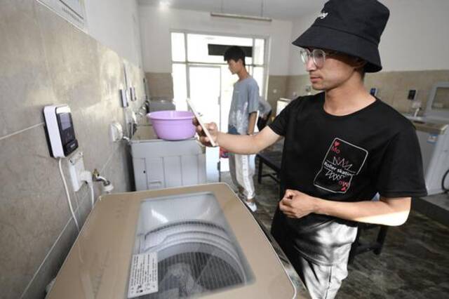 ↑宁夏建设职业技术学院学生在洗衣房通过APP扫码进行计量式用水（5月12日摄）。