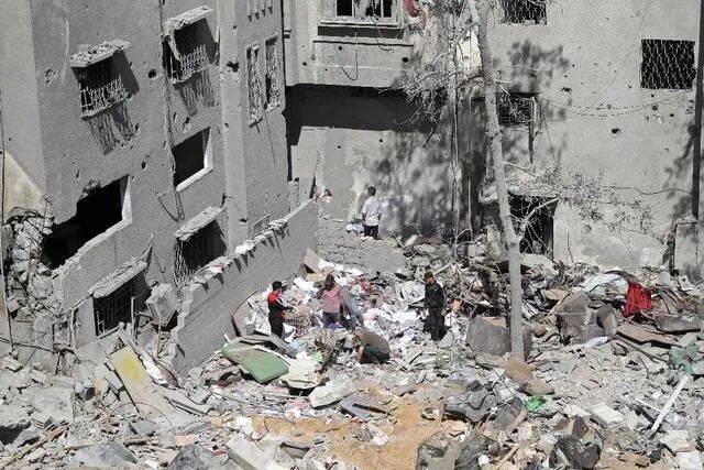 5月15日，巴勒斯坦人站在空袭过后的难民营废墟中。图源：新华社