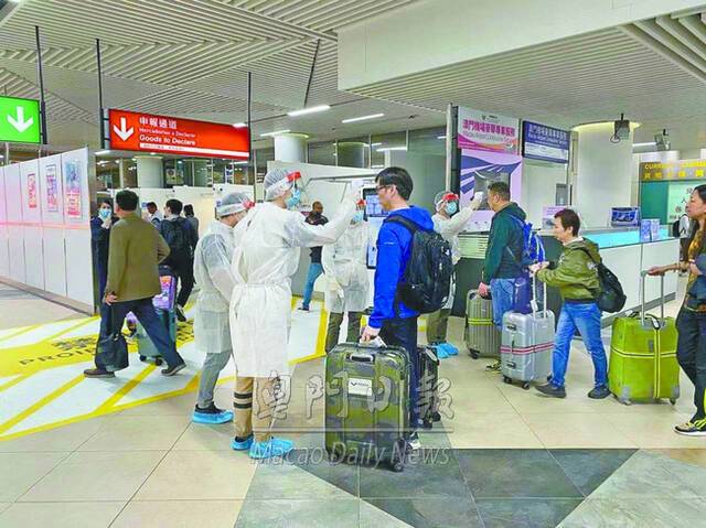 澳门机场工作人员对旅客进行测温（图源：澳门日报）