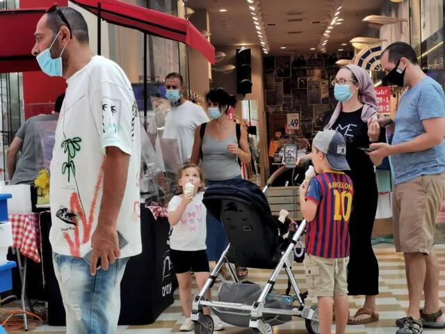 6月25日，人们戴着口罩在以色列中部城市莫迪因一座购物中心内购物休闲。图片来源：新华社发（吉尔·科恩·马根摄）