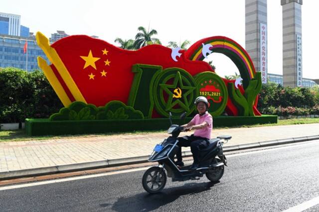 海南省海口市国兴大道前，庆祝建党百年的立体景观花坛营造出喜庆热烈的氛围，一位骑车经过的路人留下了灿烂的笑容。（海南省琼海市纪委监委杨宁摄）