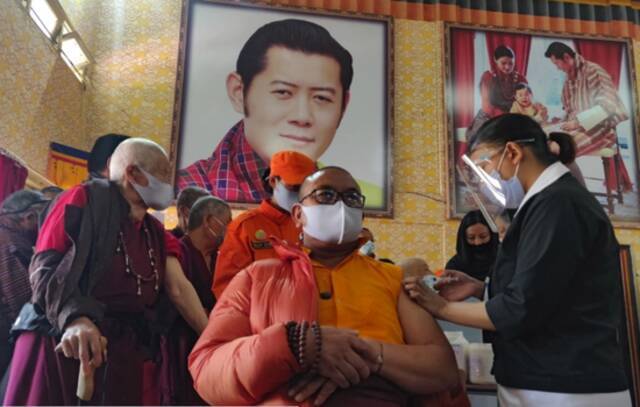 ·不丹国内疫苗接种现场，墙上还挂着旺楚克的照片。