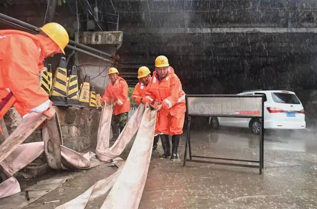 ▲7月12日，三温路铁路桥桥下，工作人员冒雨将排水带放入抽水泵中。新京报记者陶冉摄