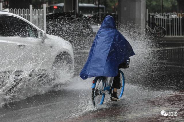 7月12日，西四环，大雨中汽车驶过积水路面，水花溅到骑车市民身上。摄影/新京报记者浦峰