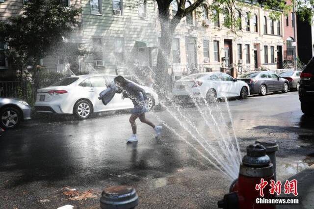 当地时间7月16日，纽约布鲁克林街道上部分消防栓喷水为市民消暑，一名女孩戏水。当日，美国纽约出现36摄氏度高温，纽约市部分街区打开消防栓喷水为市民消暑。中新社记者廖攀摄