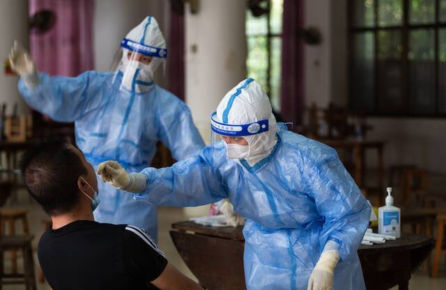 ▲18日，云南省瑞丽市勐卯镇一核酸检测点，核酸检测人员正在进行咽拭子采集工作。