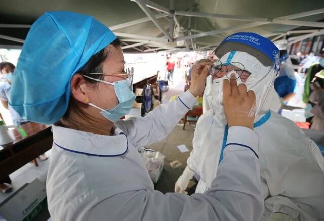 江宁区核酸检测点，工作人员在帮助身着防护服的医护人员擦汗。