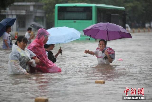7月20日，郑州经三路、农业路上，市民互相帮助走在齐腰深的积水里。图片来源：视觉中国