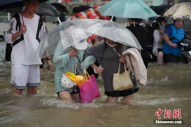 7月20日，河南郑州暴雨成灾。图为市民相互搀扶穿过积水的马路。中新社记者李超庆摄