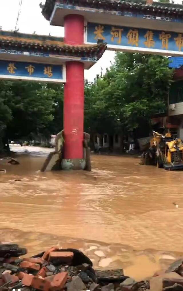 7月21日，米河镇集贸市场附近，黄色的水流正快速向前流动，没被淹没的地方堆满了砖块。受访者供图