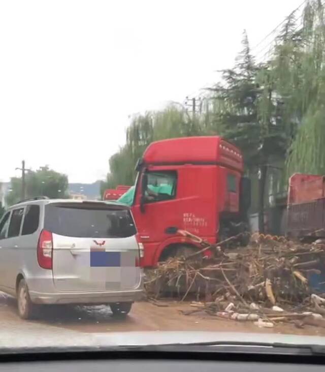 ▲7月21日，通往米北村的路旁，一辆红色大客车的车身扎进了大量树枝。受访者供图