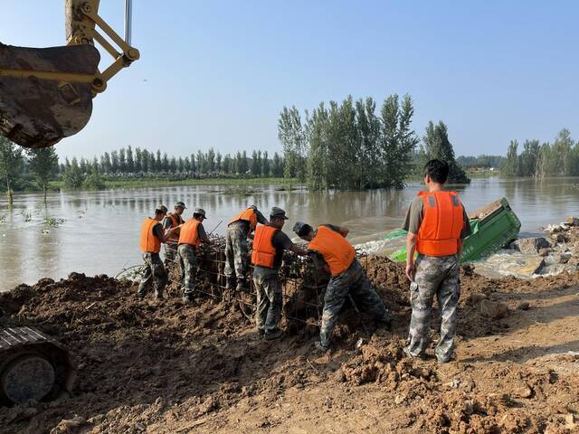  7月25日，第83集团军某工程防化旅官兵正在用铁丝固定钢笼，五个钢笼一组，投入决堤右岸。新京报记者王瑞文摄