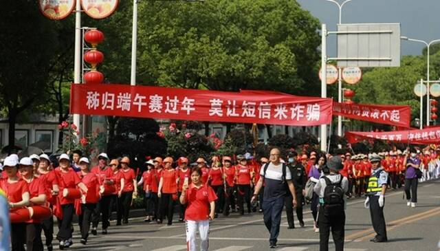 ▲2021年6月11日，在湖北省宜昌市秭归县非遗进景区的巡游队伍中，志愿者手举横幅沿途进行反电诈宣传。（视觉中国/图）