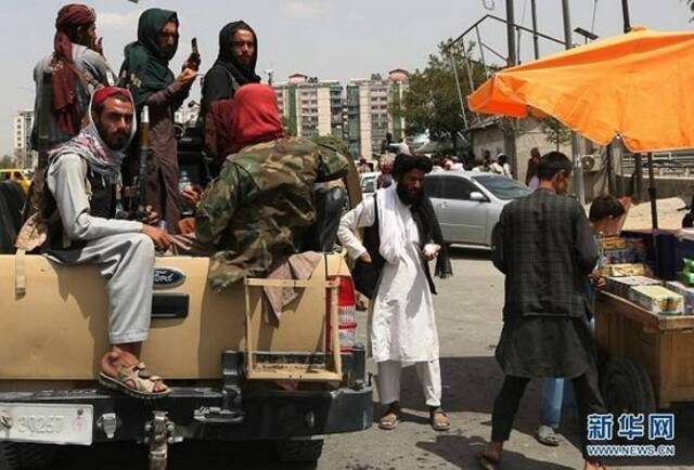 （图片说明：8月17日，阿富汗塔利班成员在喀布尔街头向小贩购物。新华社发）