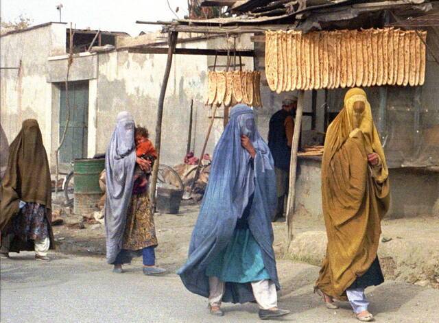 1997年11月，喀布尔。身穿蒙面罩袍的阿富汗妇女经过一家面包店。1996年9月，塔利班攻占喀布尔，建立政权。