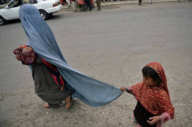 当地时间2021年8月31日，美军撤离阿富汗后，喀布尔，一个孩子拉着的妇女的罩袍在大街上行走。