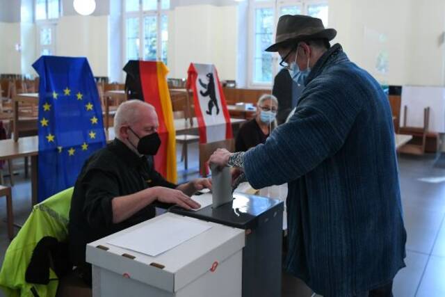 9月26日，在德国柏林一处投票站，一名选民（右）参加联邦议院选举投票。新华社记者逯阳摄
