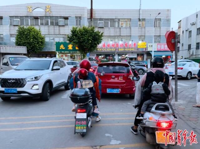 黄春花接放学的女儿回家（左），这条路上来接孩子的多数都是妈妈，她们要骑着电动车穿梭在汽车之间。中青报·中青网记者王景烁/摄