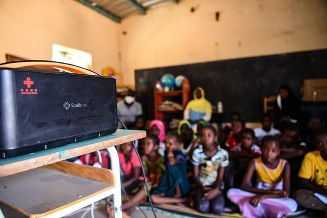 ↑11月22日，在塞内加尔达喀尔近郊的辛迪亚小学，同学们课间坐在教室的地毯上观看投影播放的动画片。新华社记者李琰摄