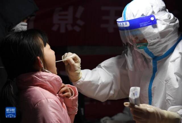 12月25日晚，在西安市莲湖区劳动路核酸采样点，医务人员为小朋友进行咽拭子采样。新华社记者李一博摄