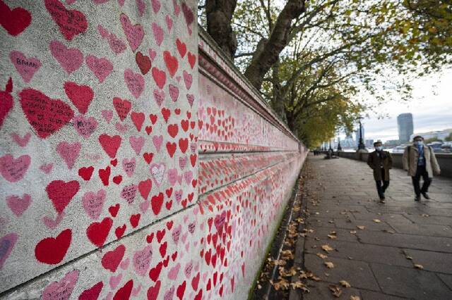 ↑2021年11月9日，人们经过英国伦敦泰晤士河沿岸的国家新冠纪念墙。新华社发（史蒂芬·程摄）