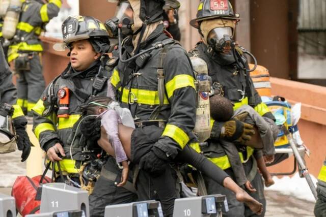 当地时间2022年1月9日，美国纽约市布朗克斯区，一栋高层公寓楼发生大火，救援人员怀抱从现场救出的孩子。图/IC photo
