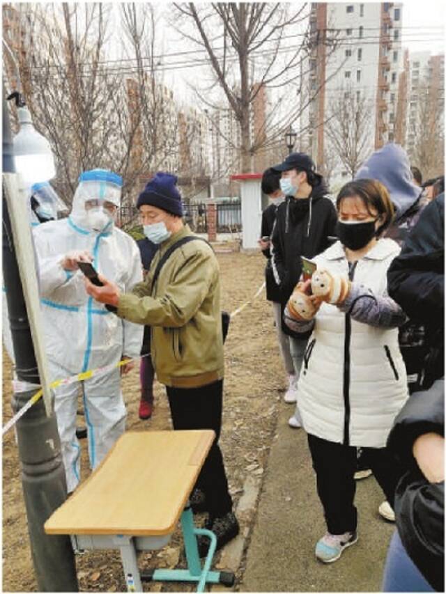 图为1月9日,天津市津南区检察院党员干警身穿防护服,在核酸检测现场维持疏导秩序,指导居民提前用手机做好检测预约登记。